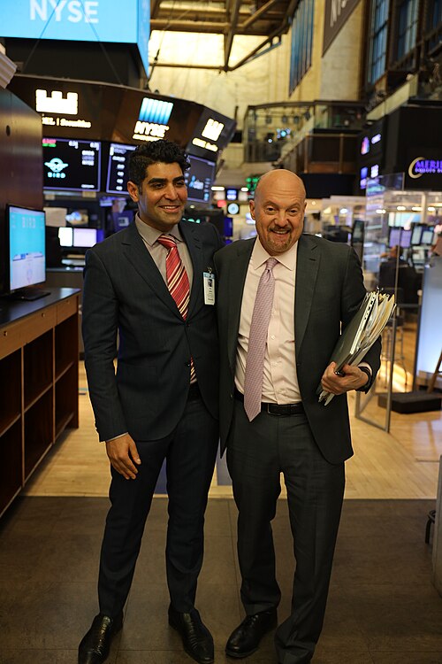 Jim Cramer on the New York Stock Exchange floor in a suit, smiling beside market monitors